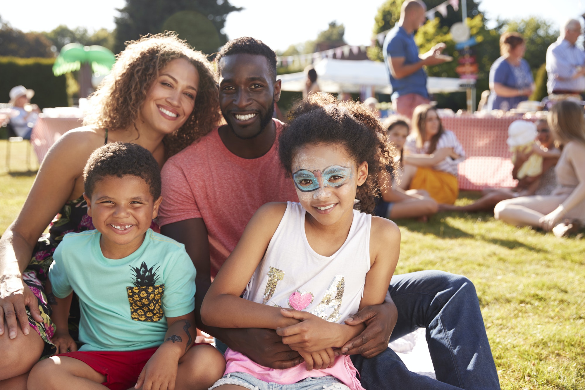 Portrait Of Family With Children Sitting On Rug At Summer Garden Fete